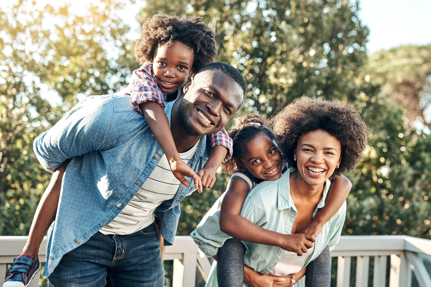 Mom and dad smile as they give their two kids piggyback rides in Estero, FL, before visiting their family dentist