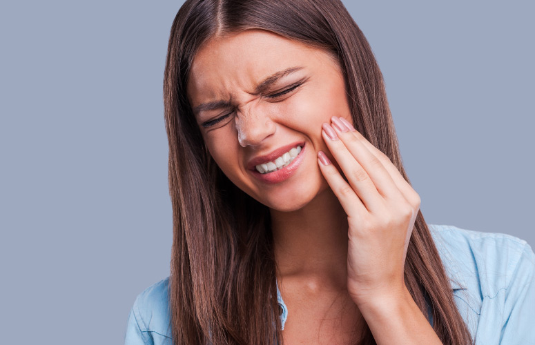 Brunette young woman cringes in pain due to pain from her wisdom teeth that need to be removed